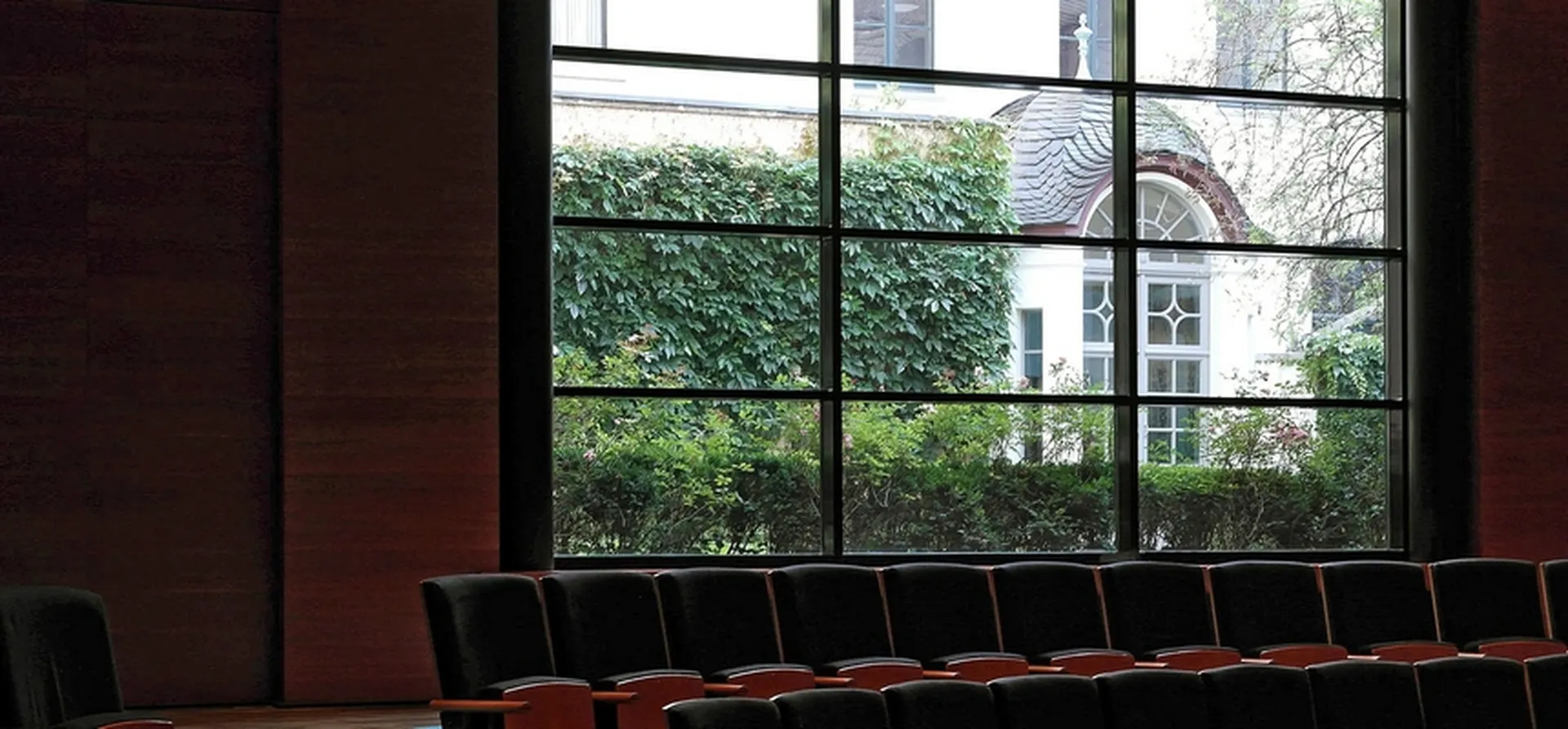 Blick durch das große, aus 12 rechteckigen Feldern bestehende Fenster des Kammermusiksaals in den Museumsgartens mit Pflanzen und Pavillon.