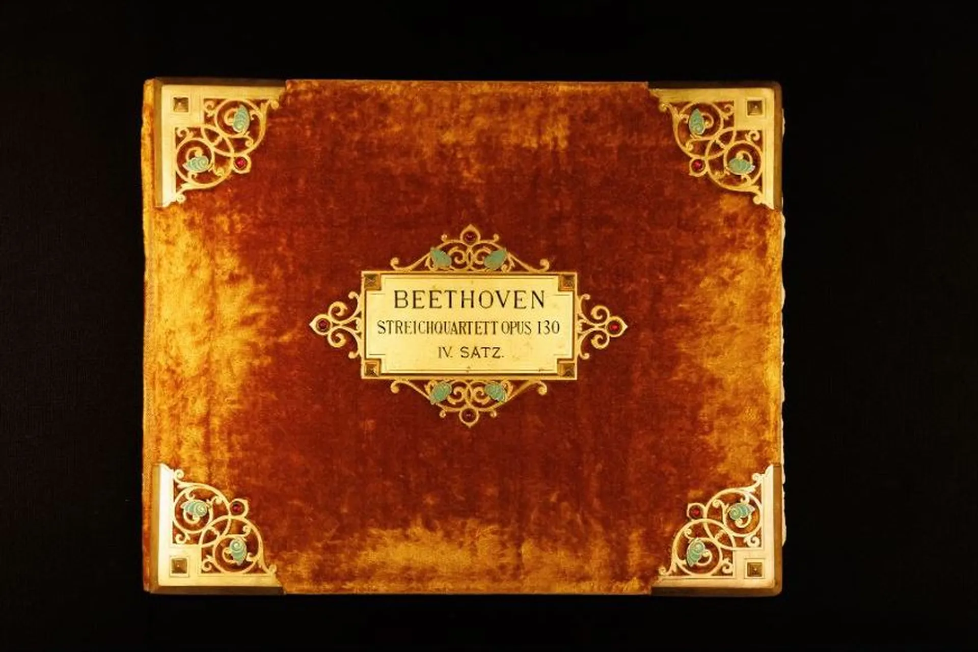 The ornate binding of the manuscript is made of amber-coloured velvet with ornamental brass fittings and glass beads on the corners and around the label.