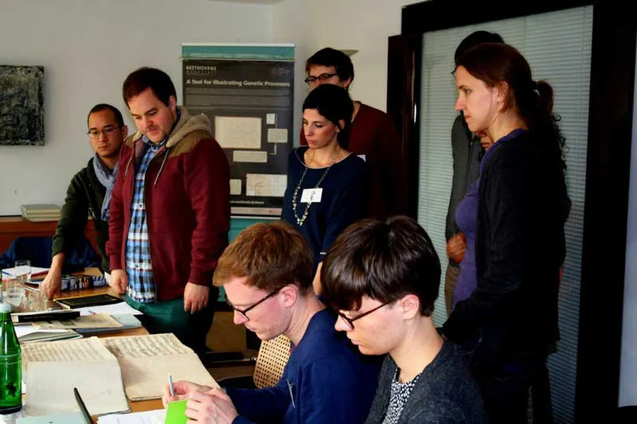 Teilnehmerinnen des Studienkollegs und angehende Wissenschaftler blicken konzentriert auf die auf dem Tisch ausgebreiteten Noten.
